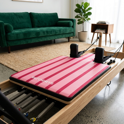 Reformys Pilates Reformer Mat in Sweet Rebel on a Pilates reformer machine inside a home lounge