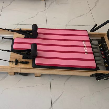 Reformys Pilates Reformer Mat in Sweet Rebel on a Pilates reformer inside a marble floor studio